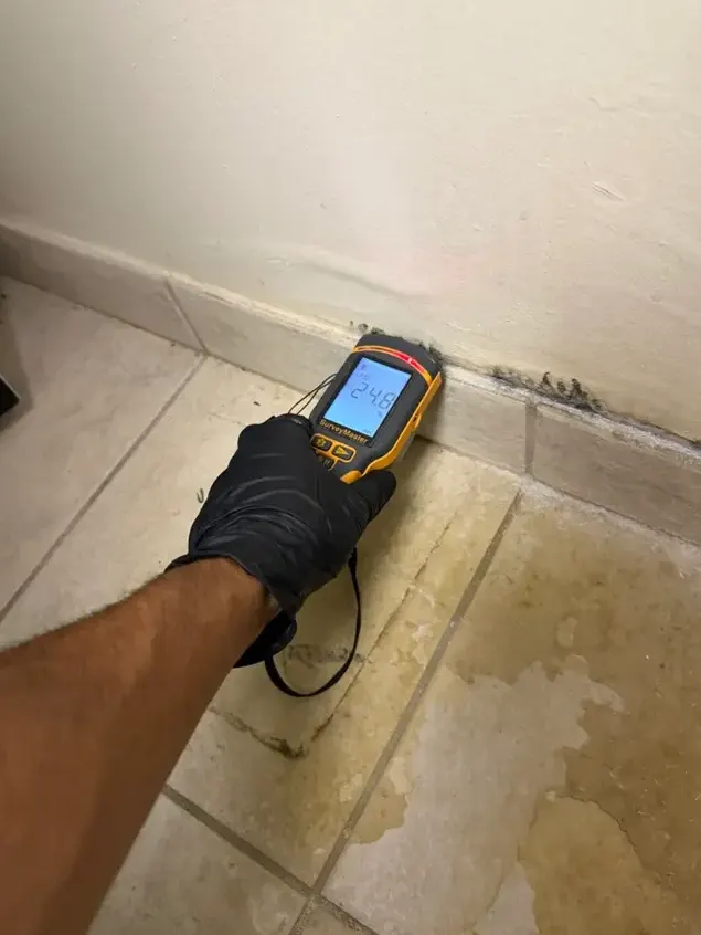 Pinless moisture meter reading a wet baseboard during a water damage inspection