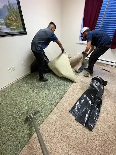 Two technicians pulling up wet carpet and pad in a bedroom